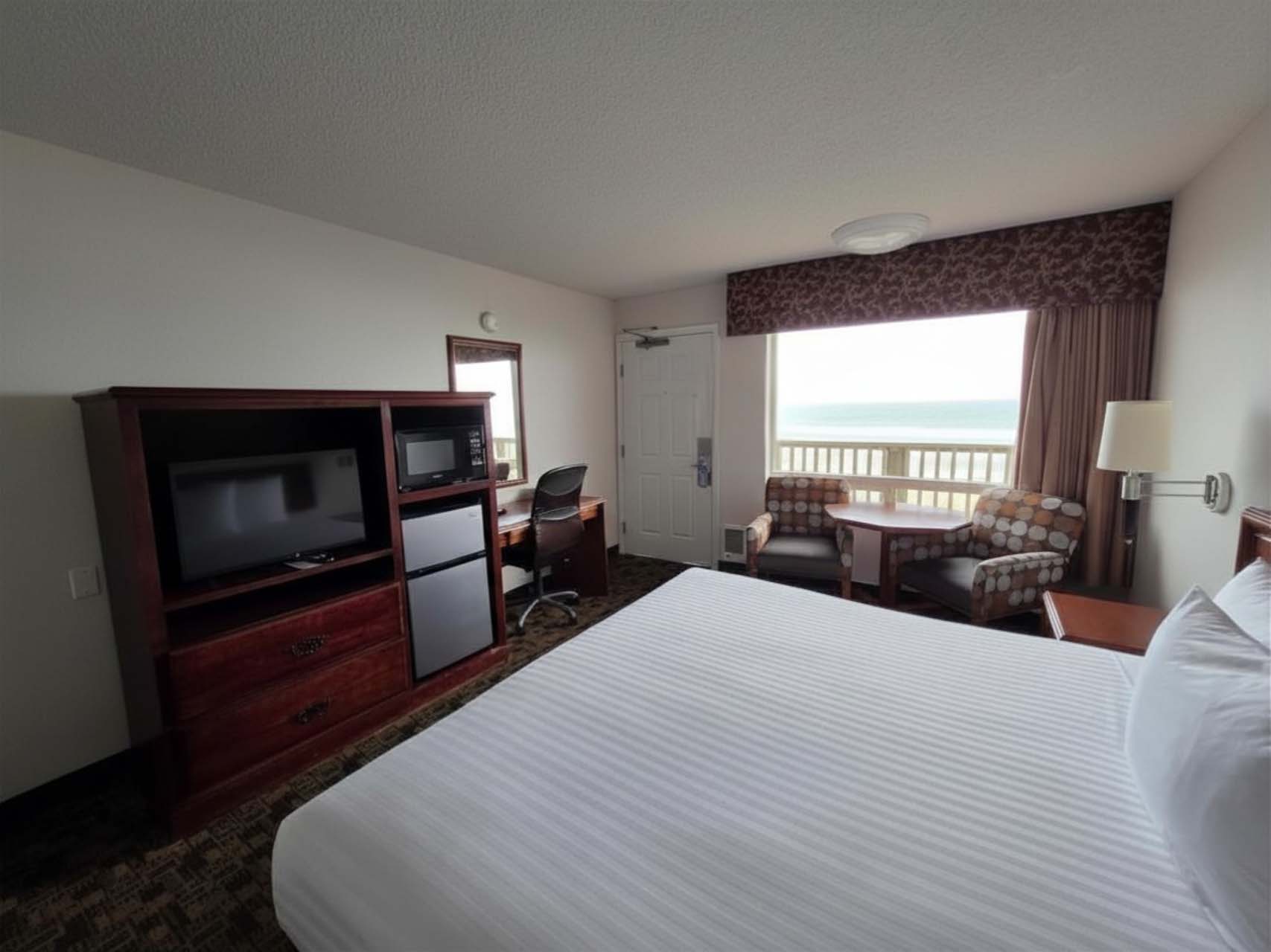 Guest room with a king bed, a TV, a desk, two armchairs, and a large window